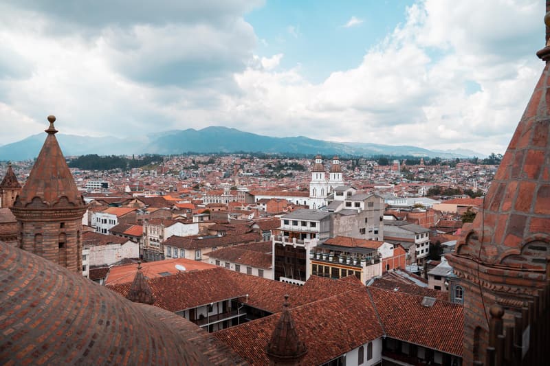 Clay-tiled rooftops of Cuenca's historic centre seen from a cathedral tower, with the Andes behind